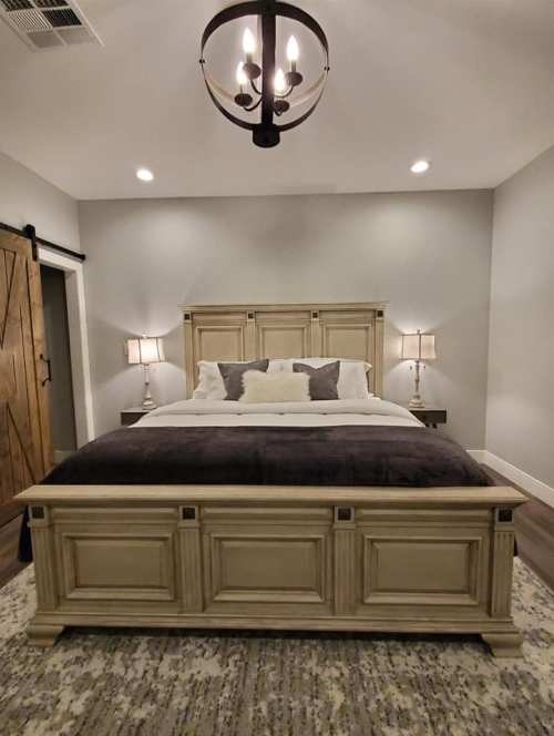 Cozy bedroom featuring a wooden bed, two lamps, and a stylish chandelier against a neutral wall.