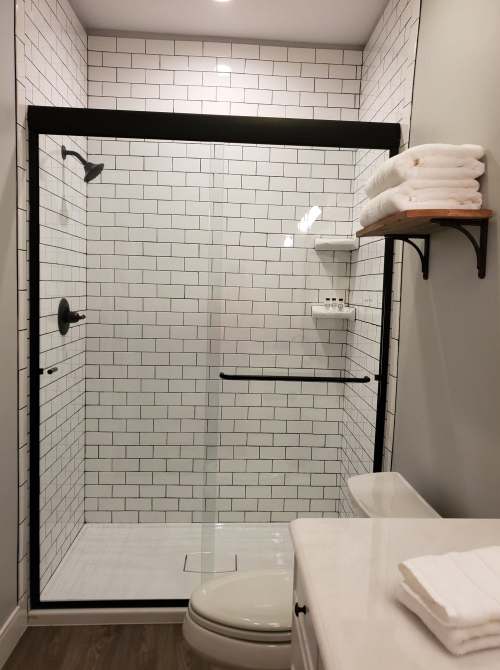 Modern bathroom featuring a glass shower with black trim, white subway tiles, and neatly stacked towels on a shelf.