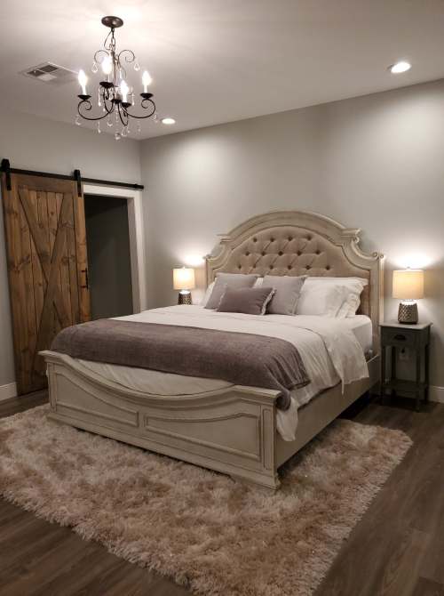 Cozy bedroom featuring a plush bed, elegant chandelier, and rustic sliding barn door. Soft rug adds warmth.