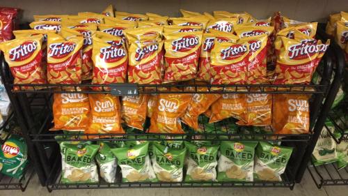 A display of snack bags, including Fritos, Sun Chips, and Lay's Baked, arranged on a store shelf.