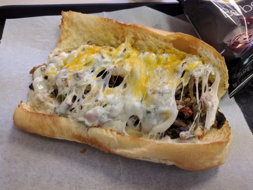A cheesy sandwich filled with meat and vegetables, served on a toasted hoagie roll.