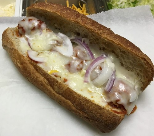A toasted sandwich filled with melted cheese, meat, and sliced onions on a white paper background.