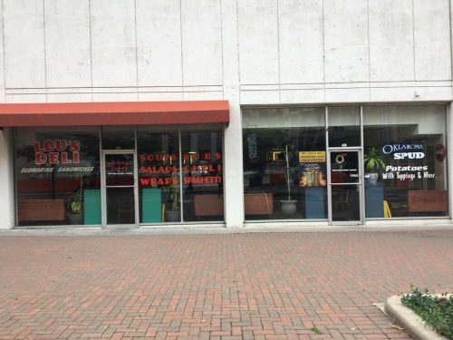 Exterior view of Lou's Deli, featuring signs for sandwiches, salads, and baked potatoes, with a brick walkway in front.