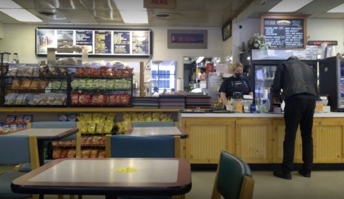 A cozy diner interior with snack displays, a counter, and a customer interacting with staff.