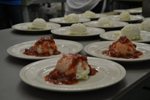 Plates of rice topped with a red sauce, arranged neatly on a table in a kitchen setting.