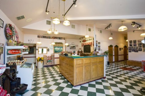 Interior of a quaint shop featuring a wooden counter, checkered floor, and vintage decor on the walls.