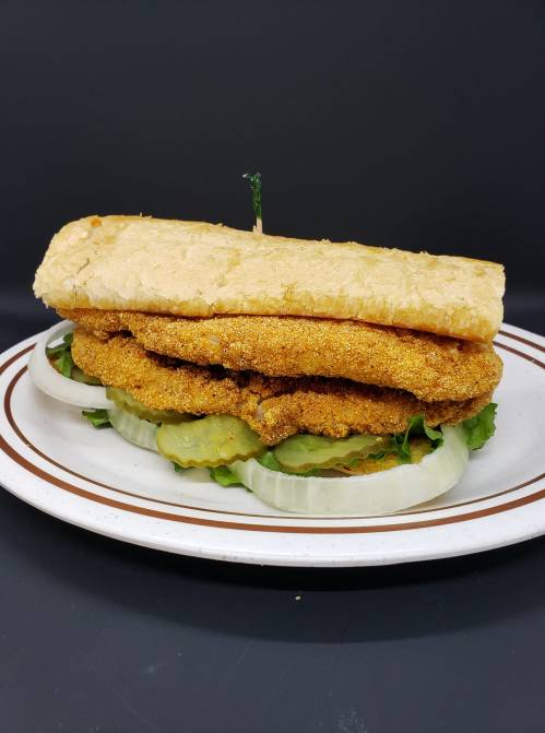 A sandwich with two crispy fried fillets, lettuce, cucumber, and a soft bread roll, served on a plate.