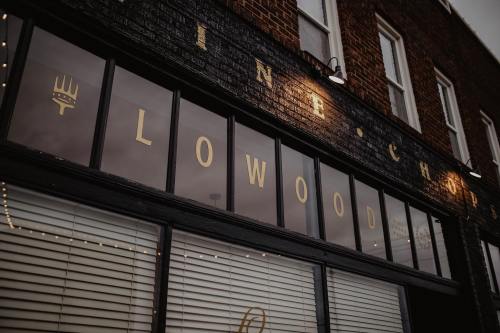 Sign of a restaurant with the name "Lowood" displayed in gold lettering on a dark brick facade.
