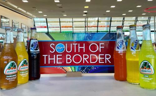 Colorful bottles of Jarritos and Fanta arranged around a sign reading "South of the Border" in a bright store setting.