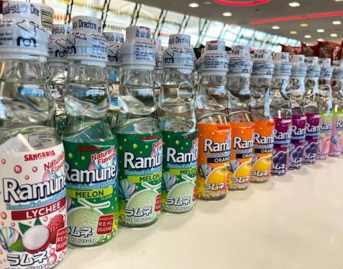 A colorful display of Ramune soda bottles in various flavors, lined up on a store shelf.