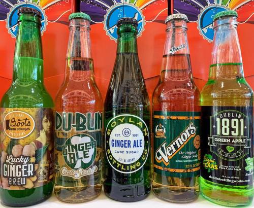 Five colorful glass bottles of different ginger ales and sodas, displayed against a vibrant background.