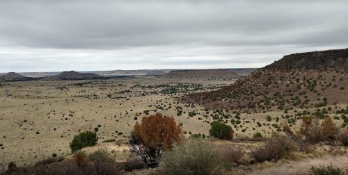 A vast, open landscape with rolling hills, sparse vegetation, and a cloudy sky in the background.