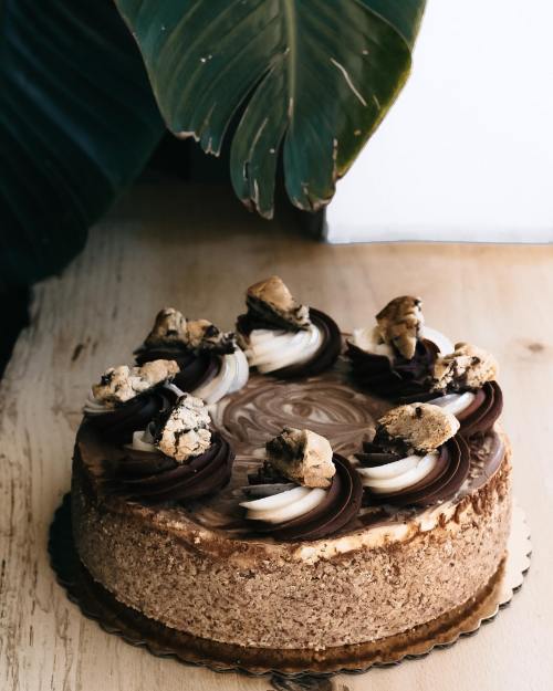 A chocolate cake topped with cookie pieces and swirls of frosting, set against a leafy background.