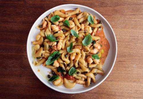 A plate of pasta with shrimp, herbs, and a creamy sauce, served on a wooden table.