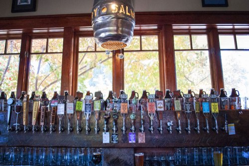 A row of beer taps with various labels, set against a backdrop of large windows and wooden decor.