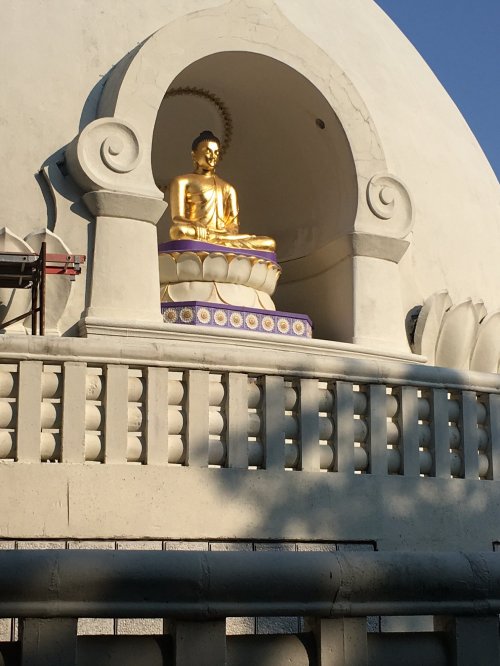 Golden Buddha statue seated in a niche, surrounded by a white dome and decorative railing under a clear blue sky.