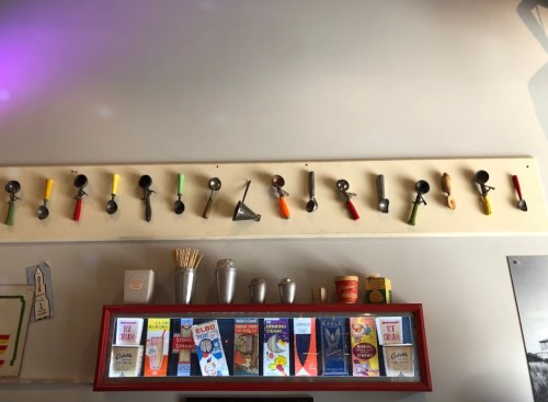 A wall display featuring various ice cream scoops and a shelf with vintage ice cream-related pamphlets and utensils.