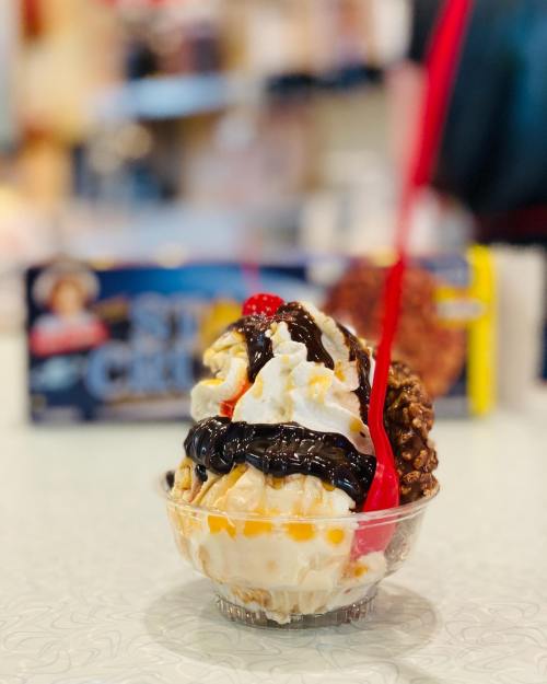 A delicious ice cream sundae topped with chocolate sauce, whipped cream, and a cherry, served in a clear cup.