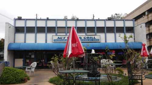 Exterior of a restaurant with a blue awning, outdoor seating, and a sign reading "Aust's Grill - Mediterranean & American Food."