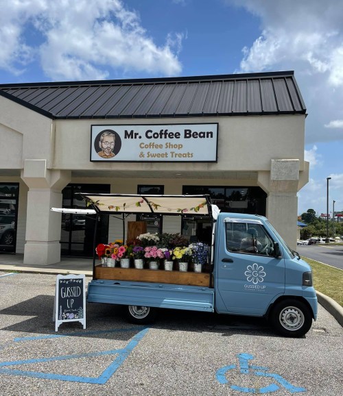 A blue truck with flowers parked outside Mr. Coffee Bean coffee shop, featuring a sign that says "Gussied Up."