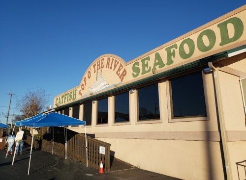 Exterior of "Catfish Top O' the River Seafood" restaurant with blue canopies and clear blue sky.