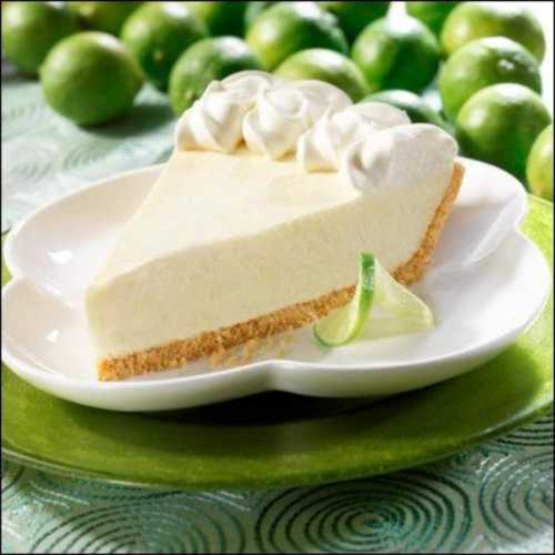 A slice of creamy lime pie topped with whipped cream, served on a white plate with fresh limes in the background.