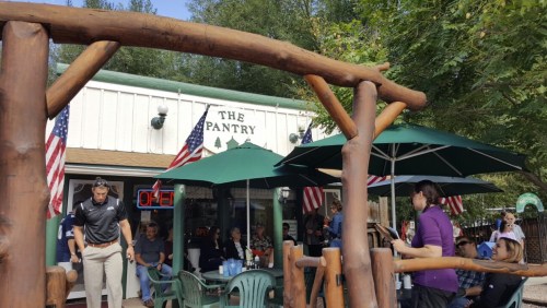 A cozy restaurant called "The Pantry" with outdoor seating, umbrellas, and American flags, bustling with patrons.