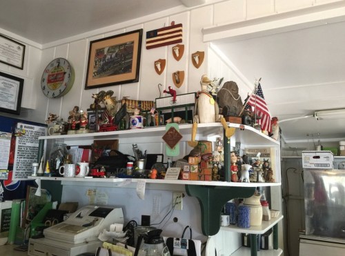 A cluttered shelf filled with various collectibles, trophies, and decorations, including flags and figurines.