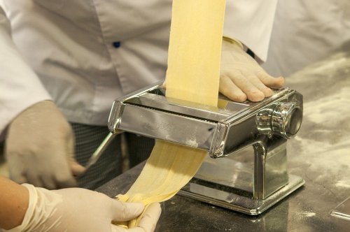A person using a pasta machine to roll out fresh pasta dough in a kitchen setting.