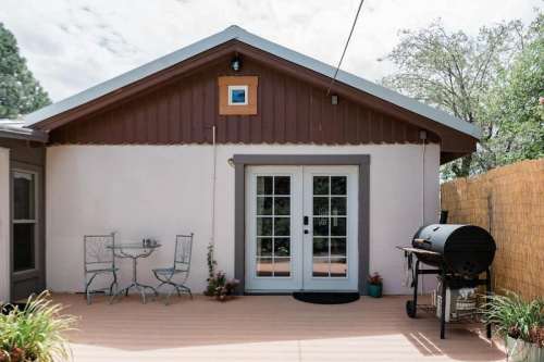 A cozy outdoor patio with a small table and chairs, a grill, and potted plants against a backdrop of a house.
