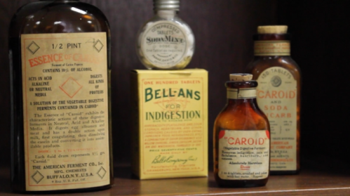 A collection of vintage medicine bottles and boxes on a shelf, labeled for various health remedies and treatments.