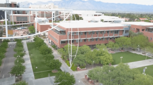 Aerial view of a campus with modern buildings, green trees, and mountains in the background.