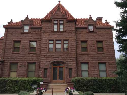 A large, historic brownstone building with a red tile roof and decorative architectural features, surrounded by greenery.