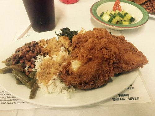 A plate of fried chicken with rice, green beans, black-eyed peas, cornbread, and a side of cucumber salad.