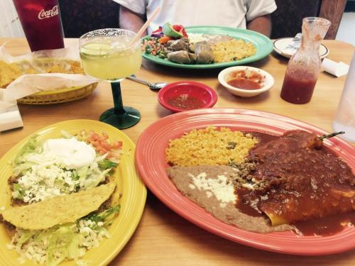A table set with colorful plates of Mexican food, including tacos, enchiladas, rice, beans, and drinks.