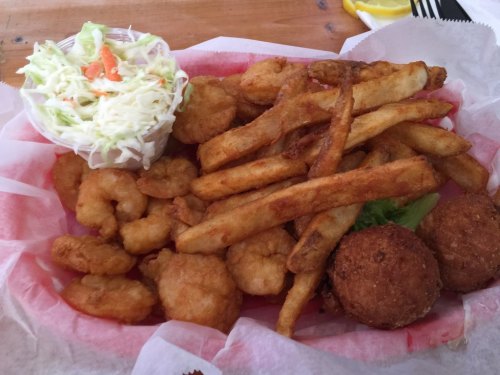 A plate of fried shrimp, French fries, coleslaw, and two hushpuppies served in a basket with pink lining.