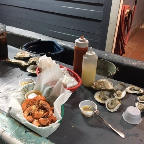 A table with a basket of shrimp, oysters, sauces, and condiments in a casual dining setting.
