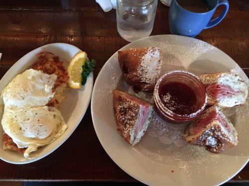 A plate with two poached eggs and a side of hash browns, alongside a plate of pastries with jam and powdered sugar.