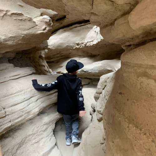 A child in a black hoodie explores a narrow, rocky canyon with high walls.