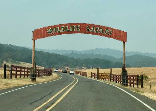 A road leads to a large sign reading "Wildlife Safari," surrounded by a grassy landscape and wooden fences.