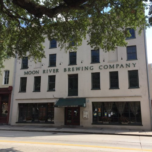 Exterior of Moon River Brewing Company, a historic building with large windows and green signage, surrounded by trees.