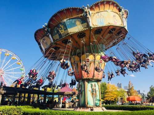 A colorful swing ride at an amusement park with people enjoying the view, surrounded by trees and a ferris wheel in the background.