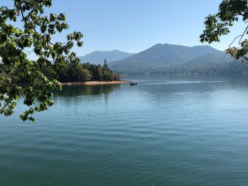 A serene lake surrounded by mountains, with a small boat on the water and trees framing the view.