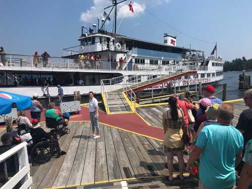 A busy dock with people boarding a large boat on a sunny day, with some in wheelchairs and others waiting in line.