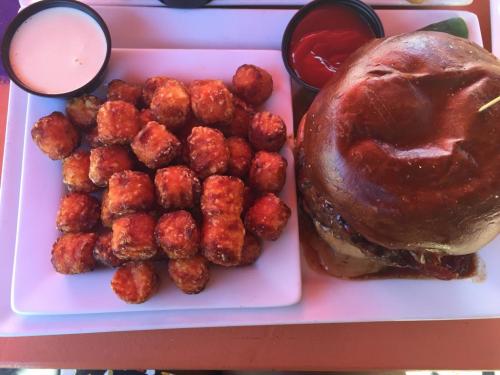 A plate with crispy tater tots and a large burger with sauce, accompanied by dipping sauces.