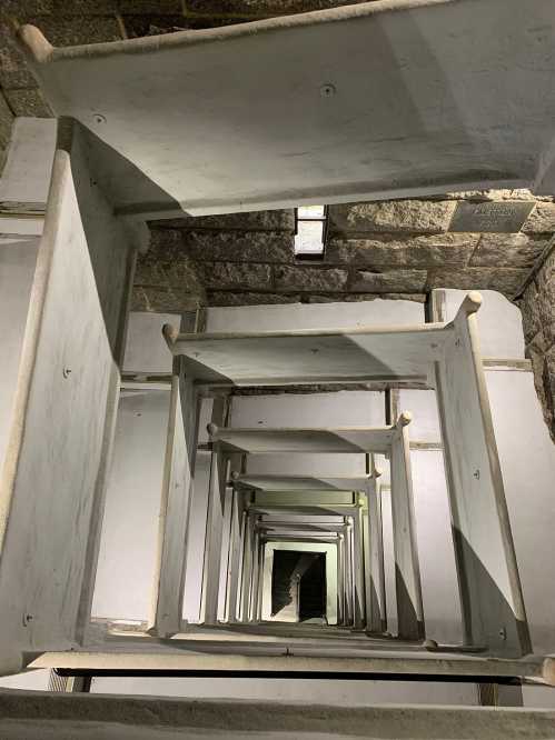 A downward view of a spiral staircase with white steps and a stone wall, creating a sense of depth and perspective.