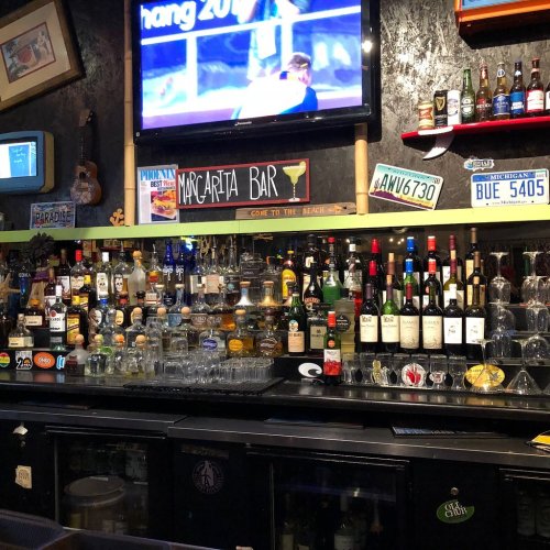 A vibrant bar with a variety of liquor bottles, a TV showing sports, and colorful signs, creating a lively atmosphere.