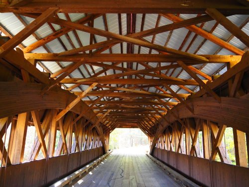 Interior view of a covered wooden bridge, showcasing its intricate wooden beams and a light-filled entrance.