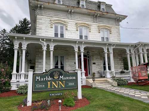 Historic Marble Mansion Inn with white stone exterior, ornate porch, and a "Vacancy" sign in front.