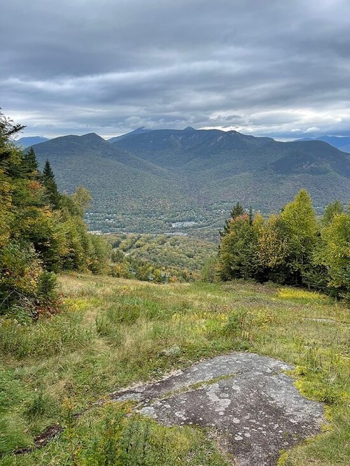 A scenic view of mountains and valleys, with lush greenery and a cloudy sky in the background.